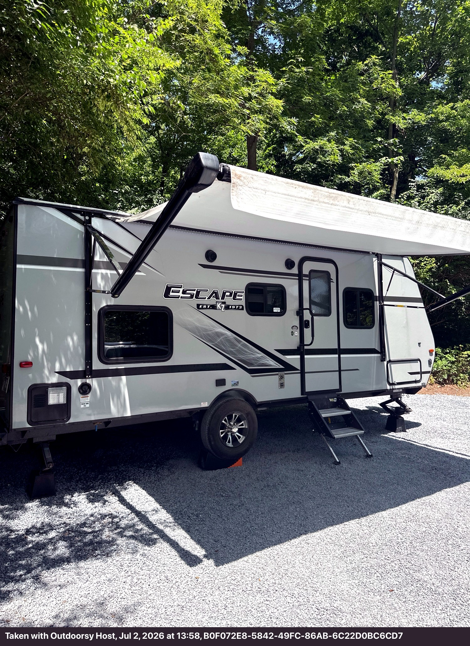 Gray 'Escape' travel trailer rv rental parked on gravel with an extended awning, ready for your next camping adventure.