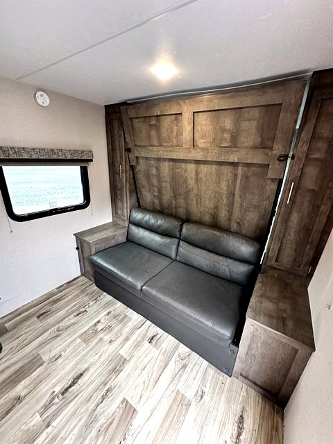 RV rental: Functional interior with a grey sofa/bed, wood paneling, overhead light, and window. Storage cabinets included.