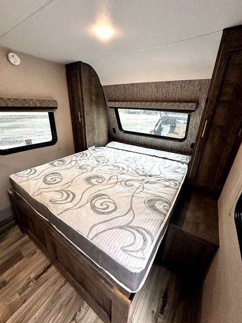 RV rental bedroom with a large bed, patterned mattress, side windows, and built-in storage cabinets.