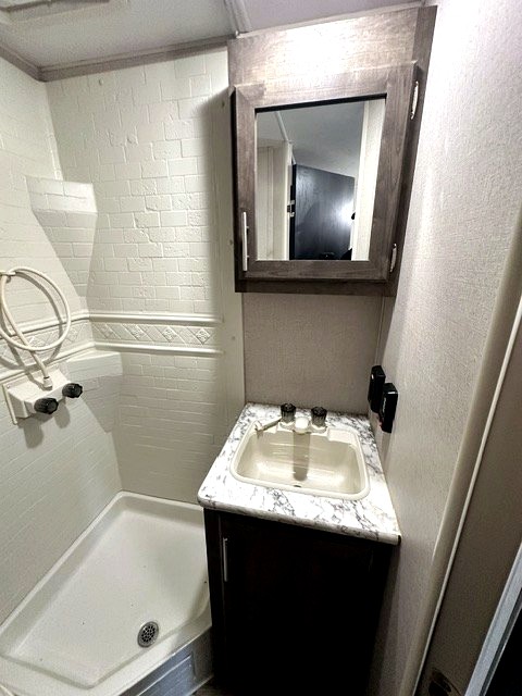 Clean RV rental bathroom featuring a shower, sink with vanity, & mirrored medicine cabinet. Perfect for your travels.