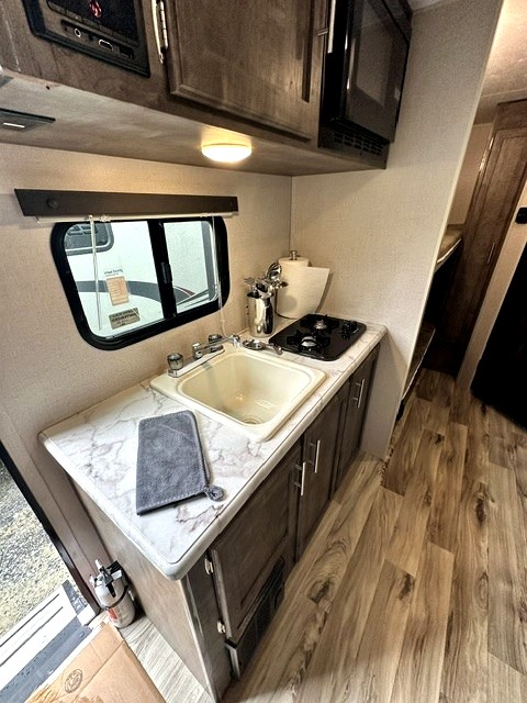 Experience our functional RV rental kitchen: sink, two-burner stove, microwave, and cabinets. Ideal for road trips!