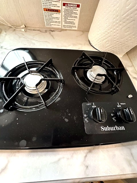 RV rental kitchen featuring a black two-burner Suburban gas stove, with essential propane safety warnings visible.