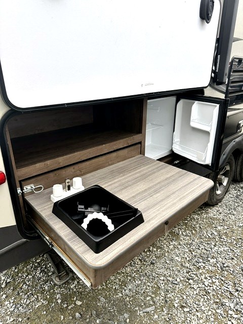 This RV rental's outdoor kitchen features a pull-out counter with a sink, storage, and mini-fridge for convenient camping.