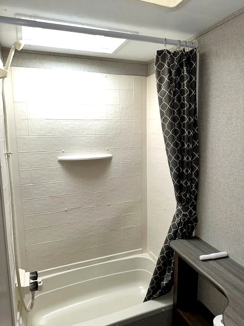 Clean RV rental bathroom with a white tub/shower, patterned grey curtain, and skylight. Ready for your next adventure.