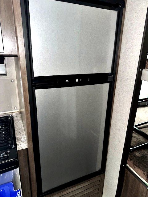 This RV rental's kitchen includes a tall, silver two-door refrigerator/freezer unit, perfect for keeping food fresh on your trip.