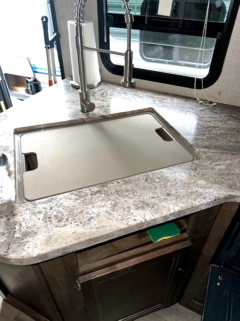Compact RV rental kitchen with a covered sink, modern pull-down faucet, and speckled laminate countertop, with a sponge in a cubby.
