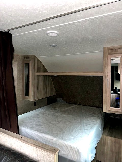 RV rental bedroom interior: queen bed with fresh cover, wood cabinets, and mirrored wardrobe, ready for use.