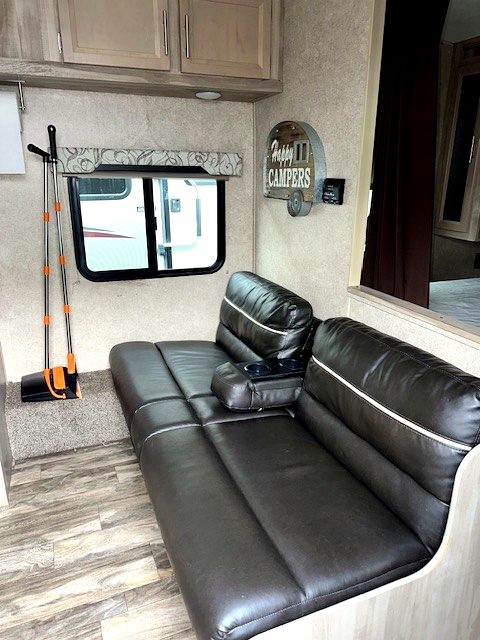 Comfortable RV rental living space with a dark convertible sofa bed, practical overhead cabinets, and "Happy Campers" decor.
