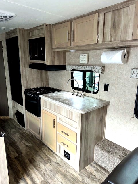 Inside an RV rental: a modern kitchen with light wood cabinets, sink, stove, microwave, and stylish wood flooring.