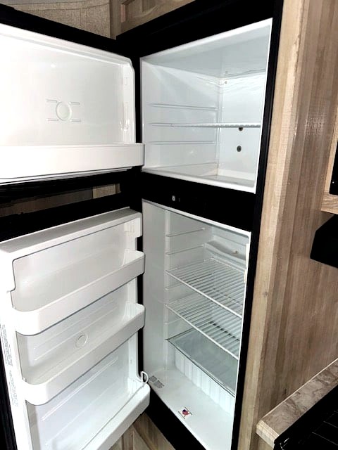 Inside a clean, empty refrigerator in an RV rental, showing the open freezer and fridge compartments with shelves.