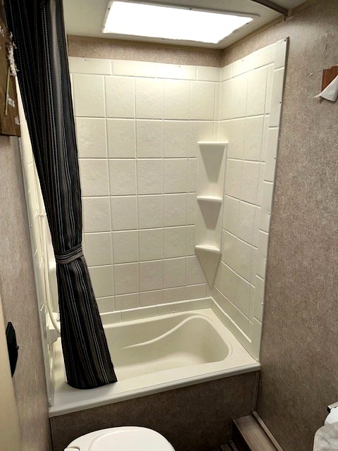 RV rental bathroom featuring a compact shower/tub with a striped curtain, corner shelves, and an overhead skylight.
