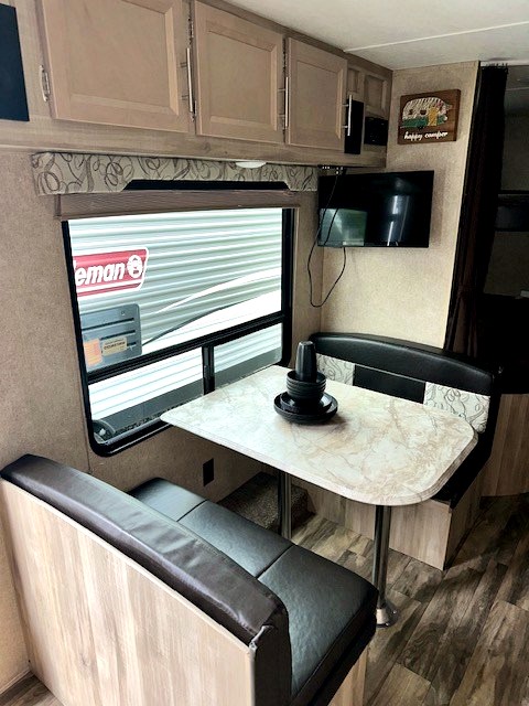 Dinette area in an rv rental, showing a table, dark benches, window, overhead cabinets, and a wall-mounted TV.
