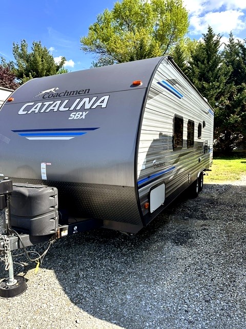 Sleek gray Coachmen Catalina SBX travel trailer for rv rental, with blue accents, parked on gravel. Ready for adventure!