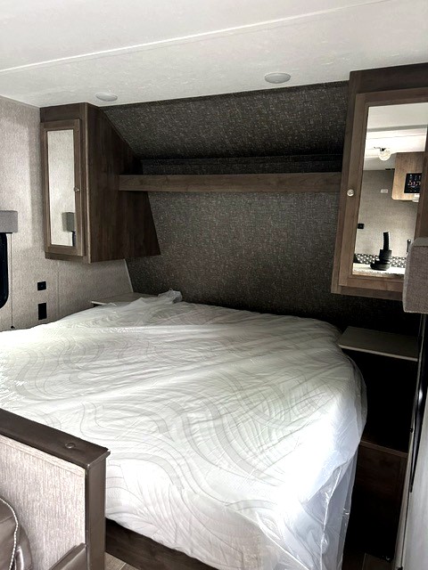 Cozy RV rental bedroom featuring a mattress in plastic, overhead storage, and built-in nightstands for comfort.