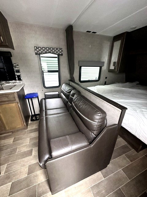 RV rental interior: cozy living area with a brown sofa, bed, and small kitchenette area, featuring patterned flooring.