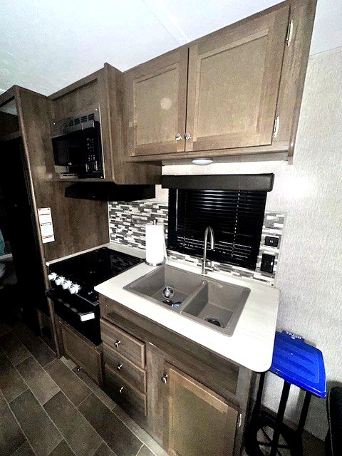 Compact RV rental kitchen with microwave, stove, double sink, and modern cabinetry, ready for your travels.