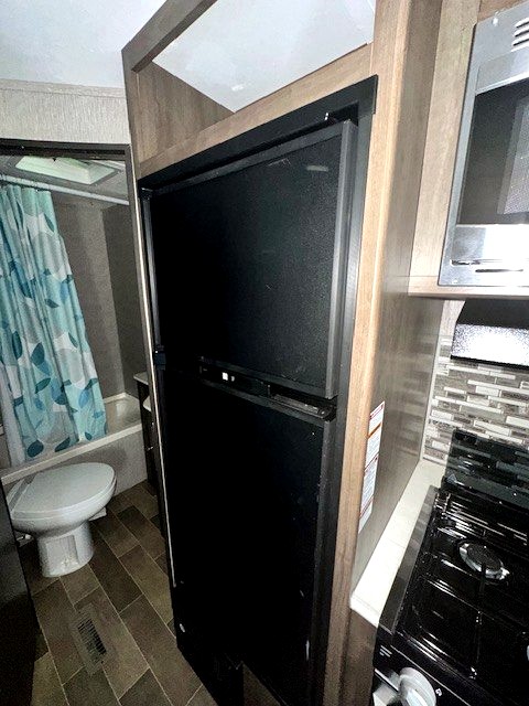 RV rental interior featuring a compact kitchen with fridge, microwave, stove, and a bathroom with toilet and shower.