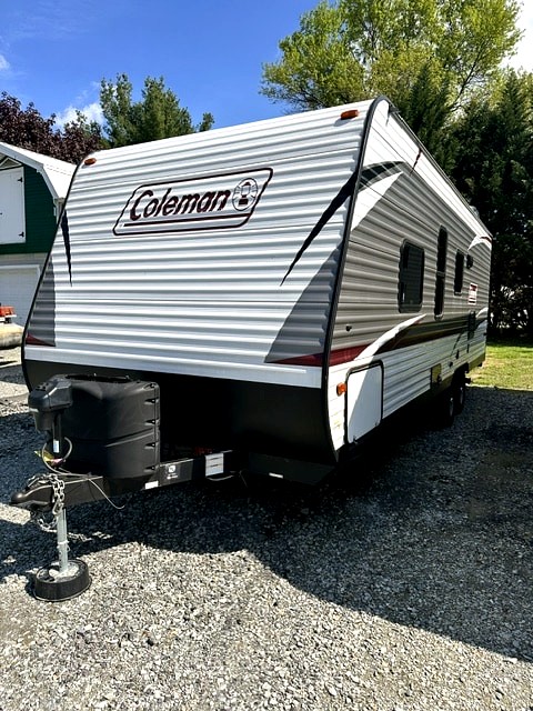 Spacious Coleman travel trailer, ready for your next RV rental adventure! White & grey exterior, parked on gravel for outdoor leisure.