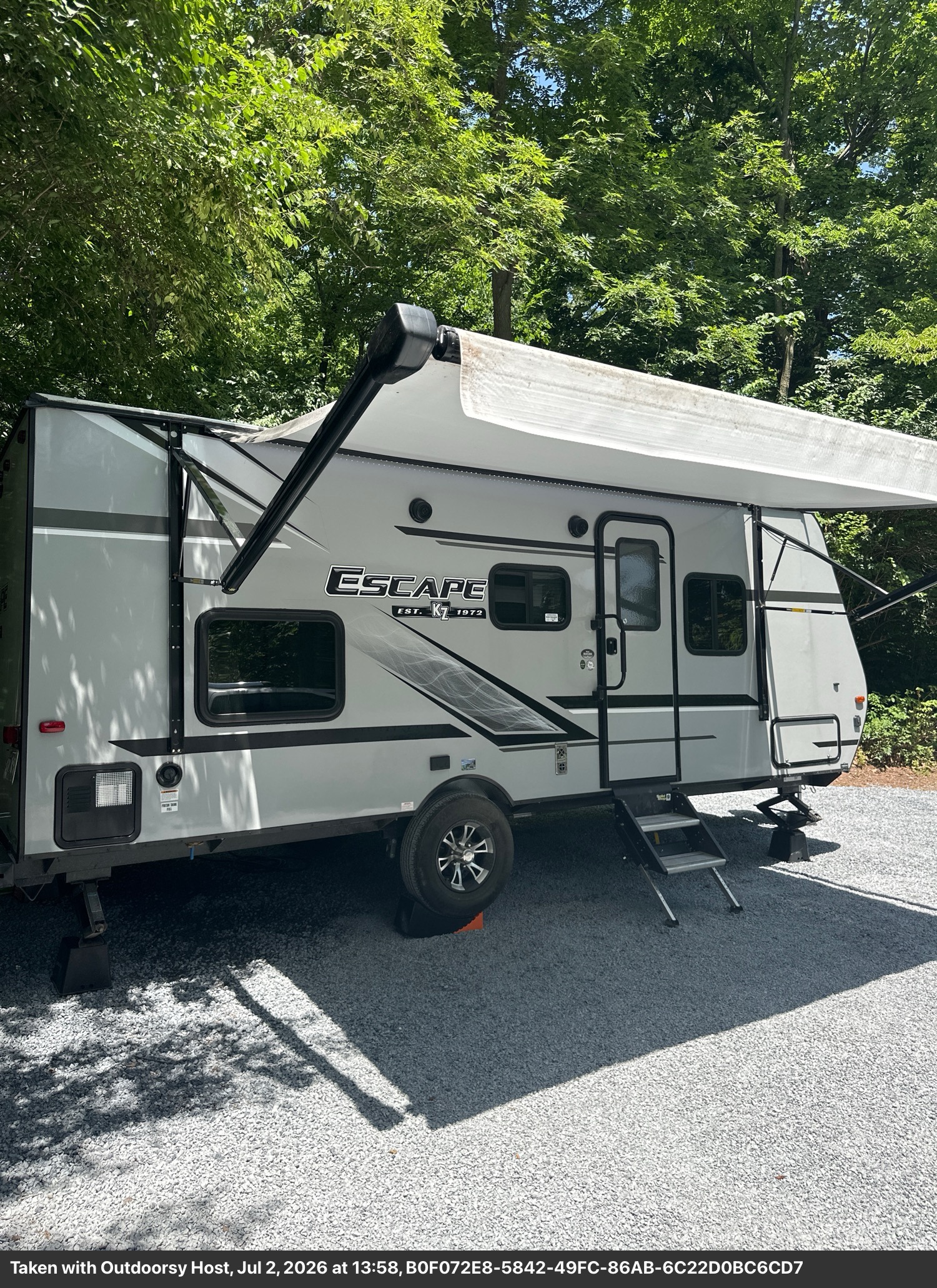 Gray 'Escape' travel trailer rv rental parked on gravel with an extended awning, ready for your next camping adventure.