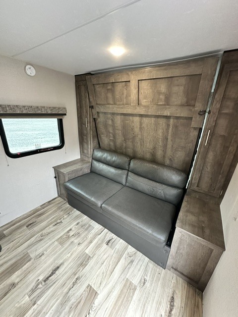 RV rental: Functional interior with a grey sofa/bed, wood paneling, overhead light, and window. Storage cabinets included.