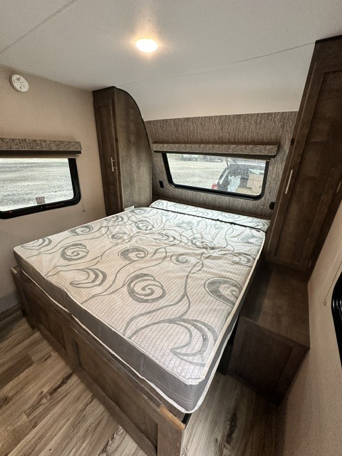 RV rental bedroom with a large bed, patterned mattress, side windows, and built-in storage cabinets.