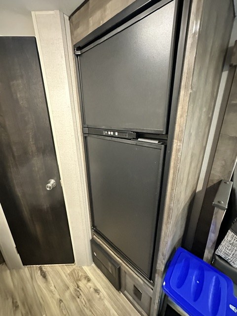 This RV rental interior features a black two-door refrigerator, a dark door, and wood-look flooring.