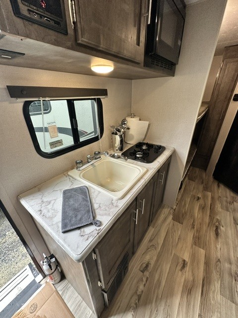 Experience our functional RV rental kitchen: sink, two-burner stove, microwave, and cabinets. Ideal for road trips!