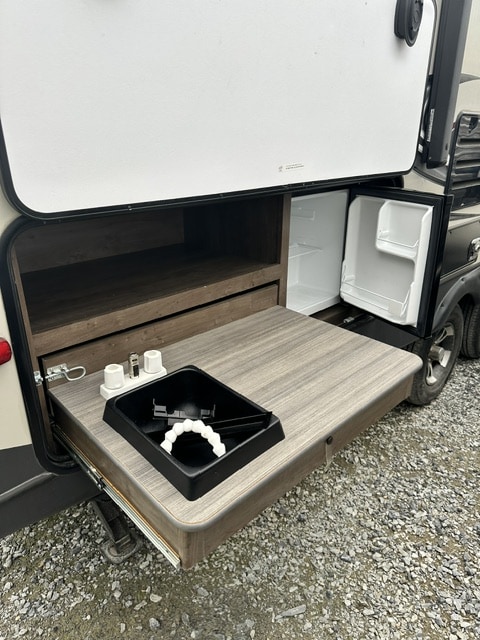 This RV rental's outdoor kitchen features a pull-out counter with a sink, storage, and mini-fridge for convenient camping.
