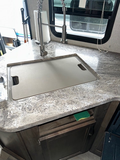 Compact RV rental kitchen with a covered sink, modern pull-down faucet, and speckled laminate countertop, with a sponge in a cubby.