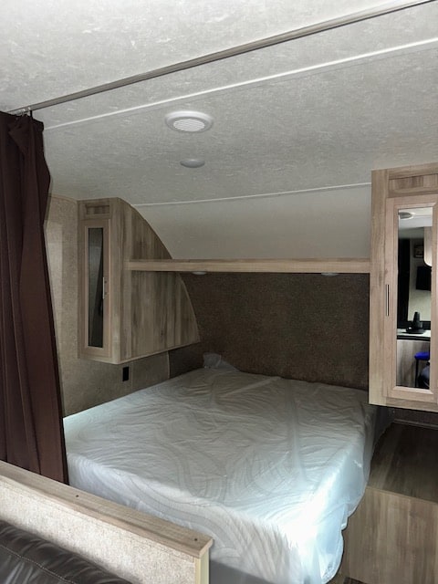 RV rental bedroom interior: queen bed with fresh cover, wood cabinets, and mirrored wardrobe, ready for use.