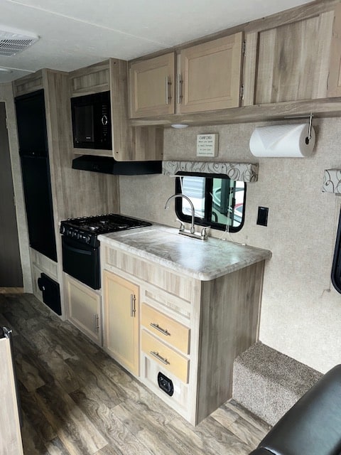 Inside an RV rental: a modern kitchen with light wood cabinets, sink, stove, microwave, and stylish wood flooring.