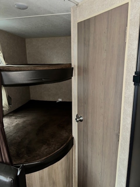 Inside an RV rental: two cozy bunk beds with dark bedding, next to a light wood door. Ideal sleeping for campers.