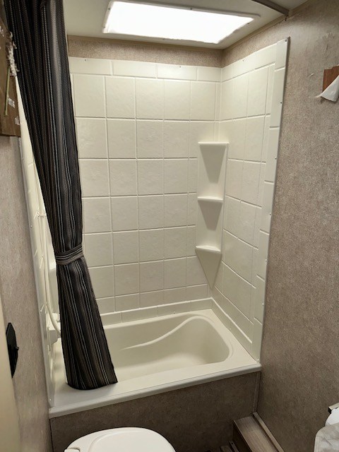 RV rental bathroom featuring a compact shower/tub with a striped curtain, corner shelves, and an overhead skylight.