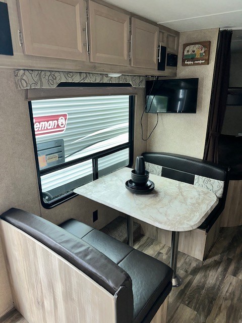 Dinette area in an rv rental, showing a table, dark benches, window, overhead cabinets, and a wall-mounted TV.