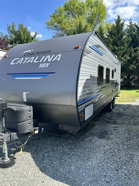 Sleek gray Coachmen Catalina SBX travel trailer for rv rental, with blue accents, parked on gravel. Ready for adventure!