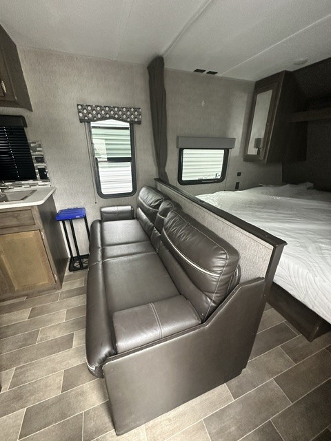 RV rental interior: cozy living area with a brown sofa, bed, and small kitchenette area, featuring patterned flooring.