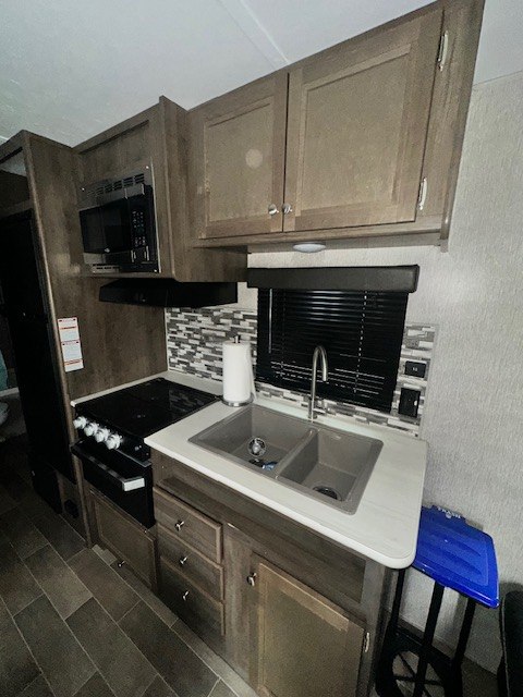 Compact RV rental kitchen with microwave, stove, double sink, and modern cabinetry, ready for your travels.