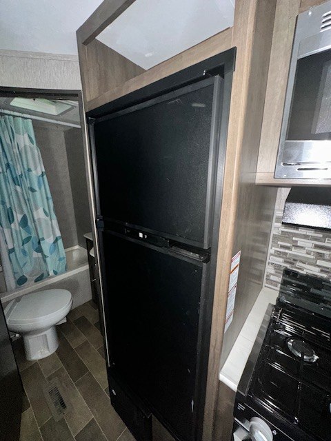 RV rental interior featuring a compact kitchen with fridge, microwave, stove, and a bathroom with toilet and shower.
