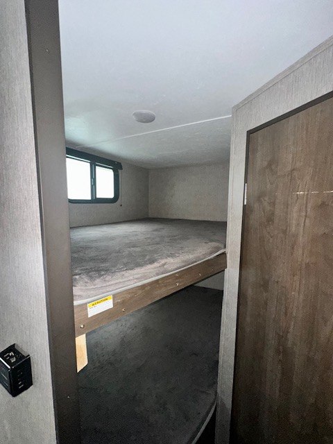 View of an RV rental's bunk bed area, featuring two cozy bunks with grey mattresses, a window, and overhead speaker.