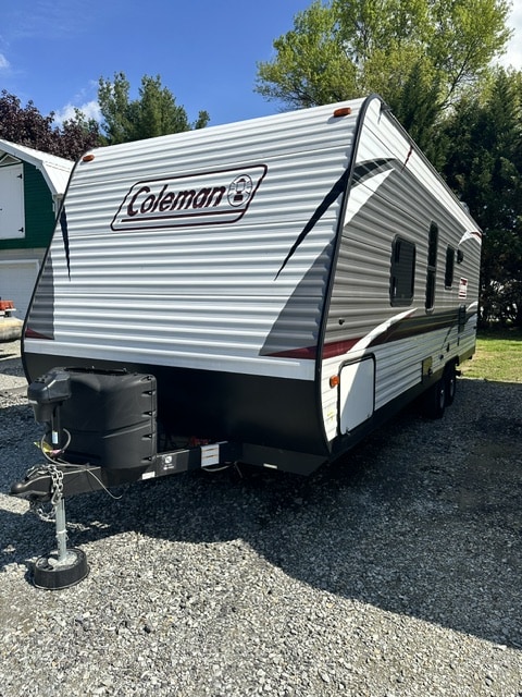 Spacious Coleman travel trailer, ready for your next RV rental adventure! White & grey exterior, parked on gravel for outdoor leisure.