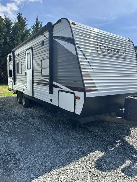 A sleek grey and white Coleman travel trailer, featuring an awning, ready for rv rental adventures on a gravel lot.